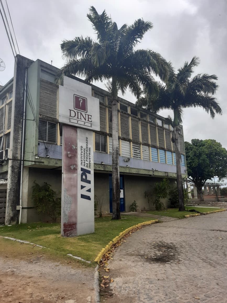 Fachada do prédio do DINE/UFPE, com o totem da diretoria e palmeiras imperiais, antes do incêndio